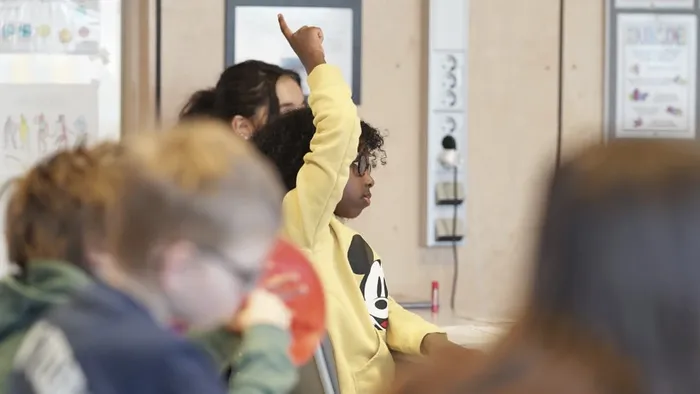 klasserom, et barn i gul genser som rekker opp hånda