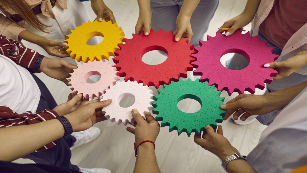 unge mennesker holder fargede tannhjul i forskjellige størrelser som symboliserer koordinert teamarbeid