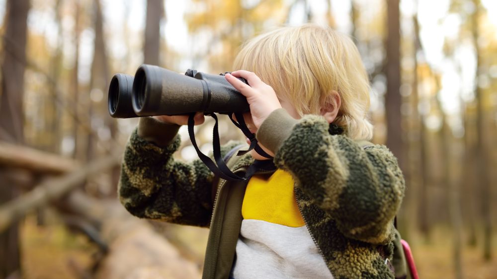 Boy on a forrest trail looking into binoculars.