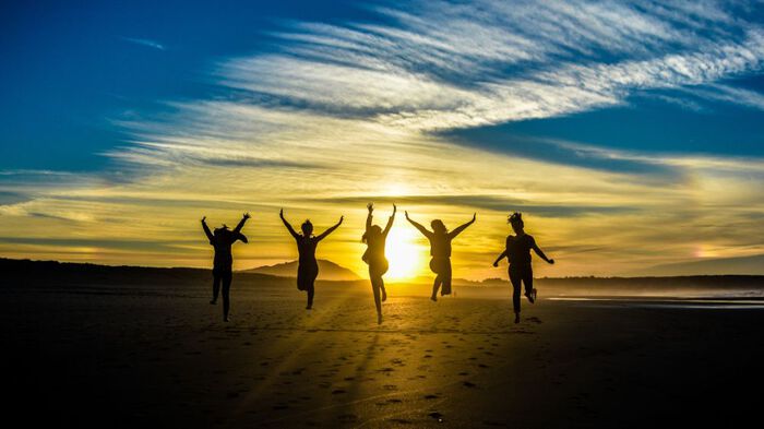 Photo illustration showing silhouettes of young people jumping un the beach at sunrise.