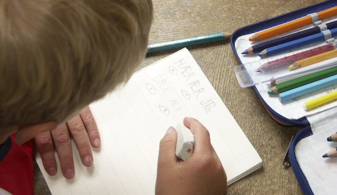 Barn (5-6 år) holder en blyant og øver på å skrive "jeg er" i en skrivebok av papir. Grunnleggende skriveopplæring.