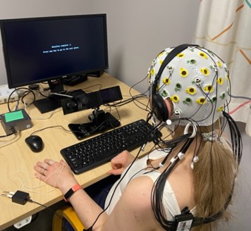 Person med EEG-hette på som ser på en dataskjerm. Et pupillkamera filmer personens øyne og en EDA-sensor er festet på personens fingre på venstre hånd. Det står et tastatur foran personen.