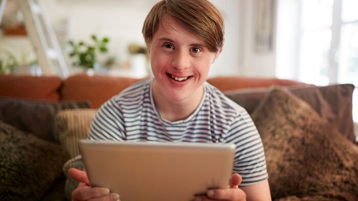 gutt med downs syndrom som sitter i sofaen blid og fornøyd med sin laptop