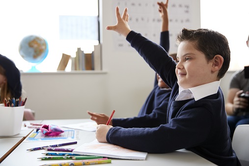 illustrasjonsfoto av gutt med down syndrom som rekker opp hånd i klasserommet