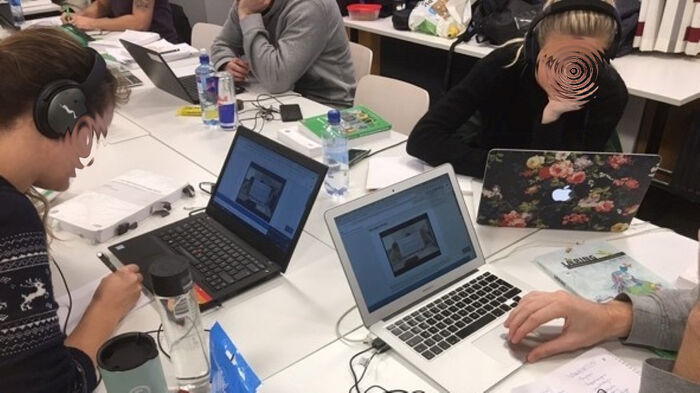 Et bilde som viser studenter som sitter ved et bord og arbeider hver for seg med eksamensoppgaver på PC.  Alle har høretelefoner 