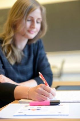 Bildet viser en student som noterer i en skriveblokk i et undervisningsrom