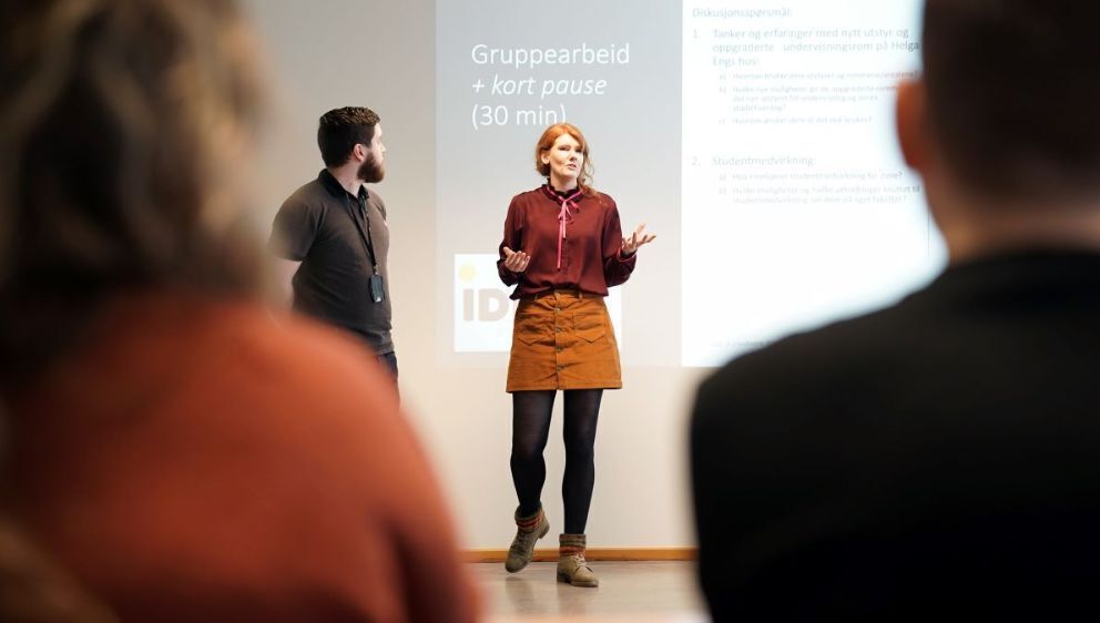 En mannlig og en kvinnelig underviser står foran en Powerpoint-presentasjon og introduserer gruppearbeid som studentmedvirkning