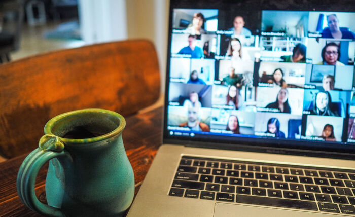 Et skrivebord med en kaffekopp og en PC-skjerm som viser deltakere i et digitalt møte.