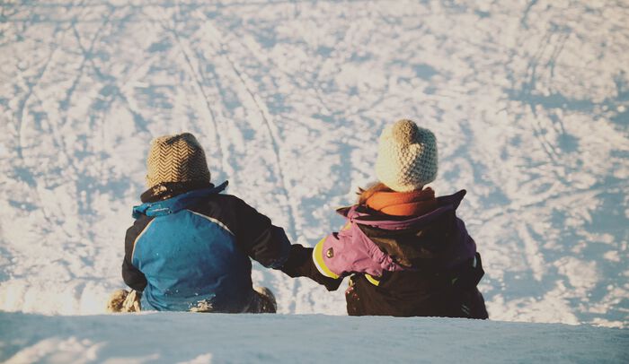To barn sitter i snøen og holder hender