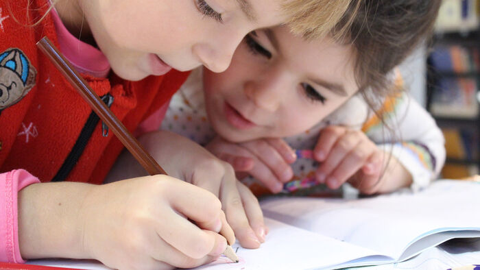 To små barn sitter tett sammen og samarbeider om en skoleoppgave.